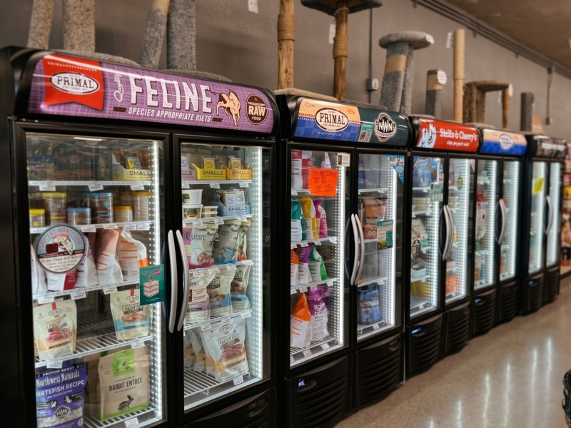 A long row of glass-door freezers stocked with raw and frozen dog and cat food